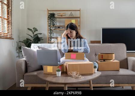 Donna asiatica sentire preoccupazione stress e mal di testa durante l'attesa di nuovo ordine dal cliente casa business venditore online Foto Stock