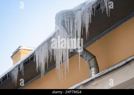 Grandi ghiacciate che pendono pericolosamente dal bordo della costruzione nella fredda giornata invernale. Diga di ghiaccio sul tetto Foto Stock