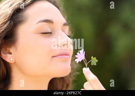 Felice donna che odora fiore in un parco Foto Stock