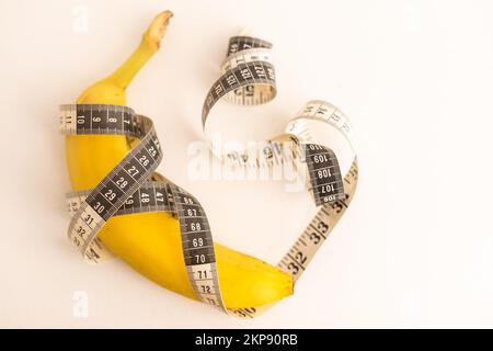 Regime, cibo sano e concetto di gestione del peso. Righello centimetrico filato intorno alla frutta fresca. Nastro giallo intorno alla banana isolato sulla luce Foto Stock