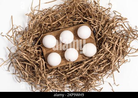 Uova di pollo su una griglia di legno e ripieno di carta su bianco Foto Stock