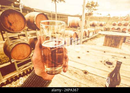 POV 1° persona orizzontale su una mano maschile che tiene un bicchiere di sidro premium quando si viaggia per le aziende vinicole di Cradoc, Tasmania meridionale, Australia Foto Stock