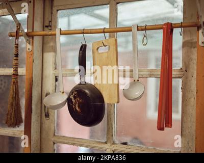 Vecchi utensili da cucina appesi al bar. Dimensioni diverse di pentole e stoviglie sul muro, decorazione casa, sfondo cucina. Foto Stock