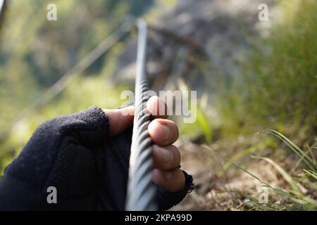 Mano che tiene una corda metallica su una via ferrata nelle alpi austriache. Foto Stock