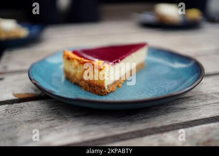 fetta di cheesecake con uno smalto di frutta lampone su un piatto blu su un tavolo di legno Foto Stock