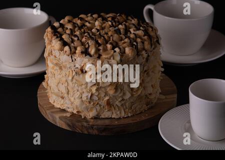 foto torta di noce rotonda con piatti tazze piattini cucchiai su sfondo nero Foto Stock