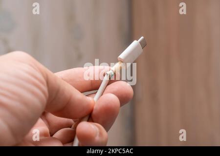 Primo piano tra il cavo del caricabatteria di tipo C bianco rotto e il telefono. Il cavo USB è danneggiato. Foto Stock