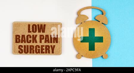 Medicina e concetto di salute. Sulla superficie bianca e blu si trovano un orologio sveglia e un segno con l'iscrizione - Low Back Pain Surgery Foto Stock