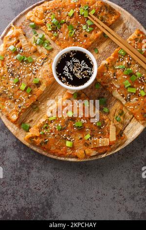 Kimchi kimchi kimchijeon in stile coreano servito con una salsa da immersione e cosparso di sesamo e cipolla verde closeup sulla tavola di legno. Foto Stock