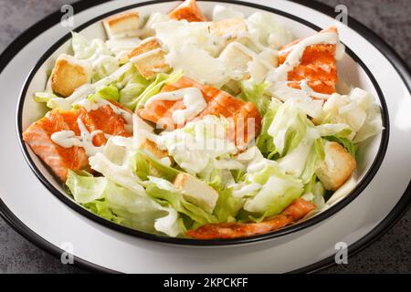Insalata Caesar di salmone alla griglia con crostini, parmigiano, condimento Caesar primo piano sul piatto sul tavolo. Orizzontale Foto Stock