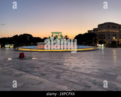 Piazza Triton, la Valletta, Malta - Gennaio 11th 2022: La Fontana Triton illuminata di sera con i resti di un cielo dorato sullo sfondo. Foto Stock