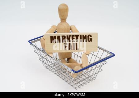 Concetto di business e finanza. Un uomo di legno si siede in un cestino di shopping, tenendo un segno nelle sue mani - il fallimento di vendita Foto Stock