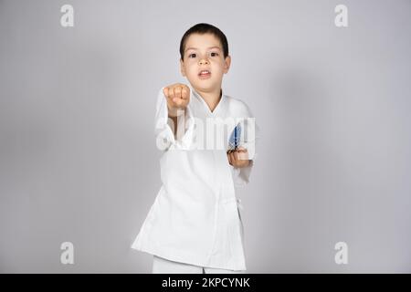 Un ragazzino in kimono pratica il karate, fa pugni con le mani in avanti. Foto Stock