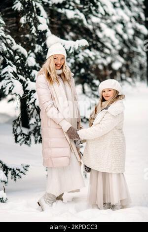 Bella madre e figlia stanno avendo divertimento all'aperto in inverno. Giocare con la neve nella foresta tra alberi nevosi Foto Stock
