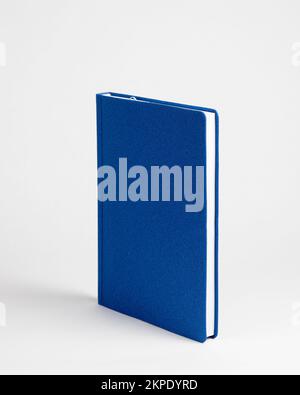 Notebook blu chiuso in una vista verticale su sfondo bianco. Vista laterale Foto Stock