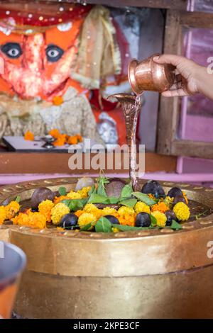 donna che offre l'acqua santa al dio indù shivalinga adorato con fiori e carta da campana al tempio Foto Stock