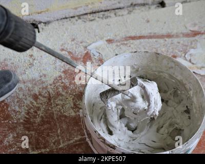 costruzione sbattere in un mortaio spesso su un secchio nel processo di riparazione, uno strumento di lavoro di un intonaco in un luogo di lavoro in una stanza Foto Stock