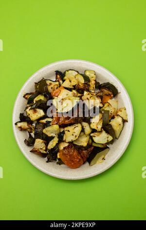 Verdure al forno miste su piatto marrone chiaro sul verde Foto Stock