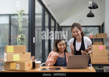 Felice due donne asiatiche imprenditore, Smile per il successo delle vendite dopo aver controllato l'ordine dal negozio di shopping online in uno smartphone a casa ufficio, concetto di Foto Stock