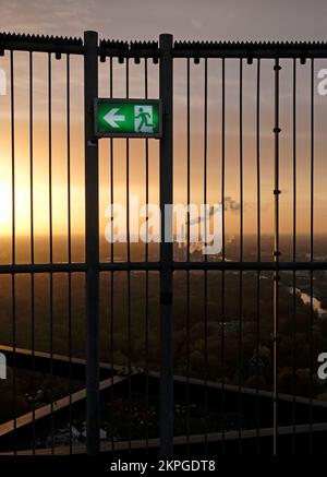 Un segnale di uscita di emergenza con un sito industriale sullo sfondo durante il tramonto Foto Stock