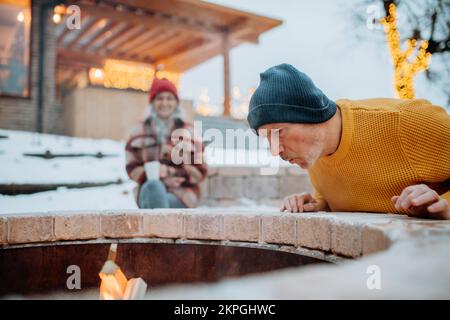 Coppia anziana seduta e riscaldamento insieme al caminetto all'aperto nella sera d'inverno. Foto Stock