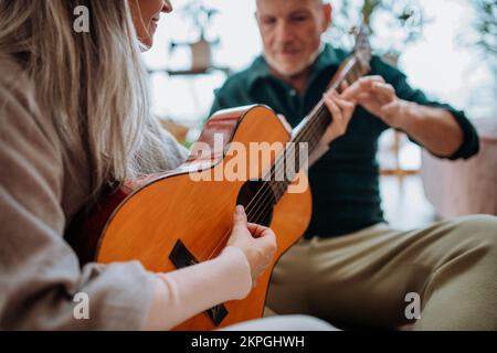 Coppia anziana che suona alla chitarra, seduto in un accogliente soggiorno e godendosi la giornata autunnale. Foto Stock