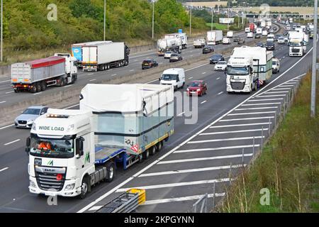 Guardando verso il basso lungo il traffico lento che fa retromarcia con i veicoli industriali e i rimorchi DAF XF carichi di merci di grandi dimensioni su strade autostradali del Regno Unito, M25 ore su 24, 7 ore su 24, 7 ore su 24 Foto Stock