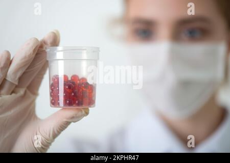 Il medico guarda le pillole in una tazza di plastica in mano. Medicina, pillole, medicina, concetto di vitamine. Primo piano, messa a fuoco selettiva. Foto Stock