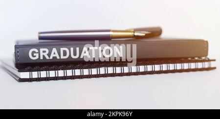 Concetto di istruzione. Sul tavolo ci sono un taccuino, una penna e un libro. Il libro dice -GRADUAZIONE Foto Stock