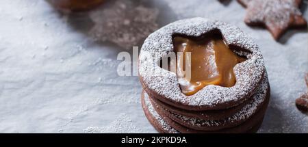 Biscotti al cioccolato Linzer con caramello salato sullo sfondo del tavolo. Natale concetto di cibo Foto Stock