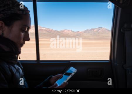 Donna all'interno di un veicolo che controlla il suo cellulare mentre passa attraverso l'Altiplano o le pianure alte, Dipartimento di Potosi, Bolivia Foto Stock