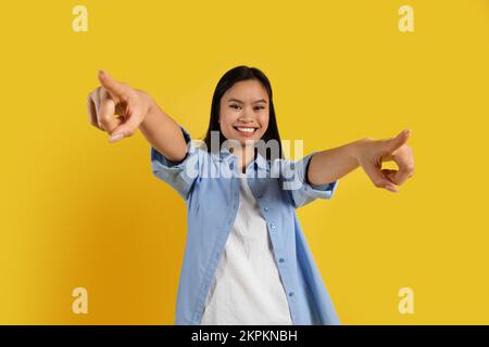 Felice fidato studente cinese donna millenario in casual punta dita alla macchina fotografica, ha divertimento Foto Stock
