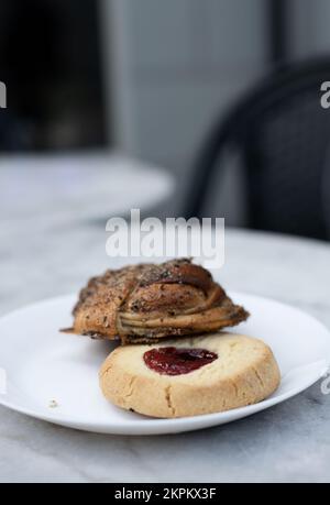 Classico biscotto di shortbread svedese, conosciuto come hallongrotta, con marmellata al centro e un panino alla cannella su un piatto. Selezione di dolci su piatto. Foto Stock