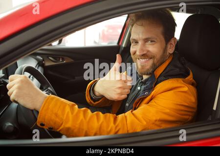 Felice uomo dai capelli rossi seduto all'interno del veicolo, sorridente, mostrando super. Foto Stock