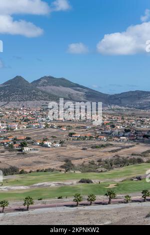 Paesaggio con campo da golf verde e villaggio su isola arida, girato in luce luminosa caduta a Porto Santo isola, Portogallo Foto Stock