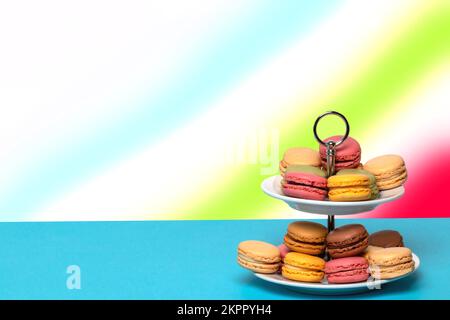 Primo piano di colorati macaroni francesi su un etagere a due piani su un tavolo blu con spazio sullo sfondo astratto dell'arcobaleno. Modello per il vostro cibo e. Foto Stock