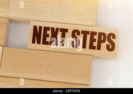 Concetto di business e finanza. C'è un Jenga di legno sul tavolo, su un Jenga è scritto - PASSI SUCCESSIVI Foto Stock