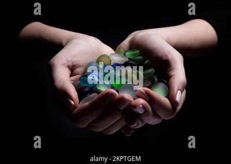 Mani con pietre colorate giovane donna sta tenendo una collezione di varie gemme minerali grezze nel suo palmo isolato su sfondo nero Foto Stock