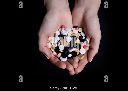 Donna mano che tiene la pillola su sfondo nero isolato Foto Stock