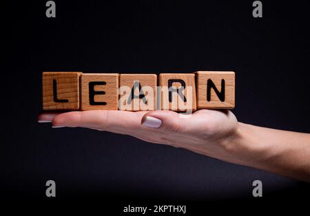 Le mani femminili tengono un cubo con lettere, cubi di legno con le parole affitto vendita, comprare e prestito. Progetto per designer su sfondo nero . Parole a casa imparare Foto Stock