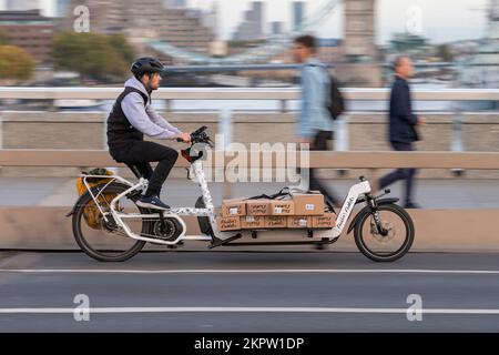 Un corriere ciclistico in sella a una bicicletta e-cargo carica di fiori, London Bridge, Londra, Regno Unito. 18 Ott 2022 Foto Stock