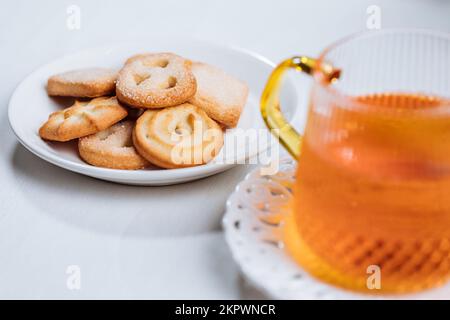 Biscotti e tè in tazza di vetro serviti nella luminosa atmosfera natalizia. Impostazione delle scene luminose e luminose. Foto Stock