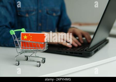 Piccolo carrello con bandiera cinese sul tavolo. Uomo che utilizza il notebook per lo shopping online. Foto Stock