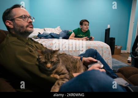Gatto siede sul giro del padre mentre gioca i video giochi con il figlio Foto Stock