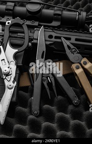 multitool moderno con molti strumenti. Accanto all'arma si trova uno strumento militare portatile multi-tasking. Forbici multifunzione. Sfondo scuro. Foto Stock