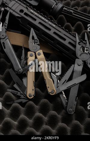 multitool moderno con molti strumenti. Accanto all'arma si trova uno strumento militare portatile multi-tasking. Forbici multifunzione. Sfondo scuro. Foto Stock