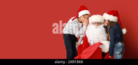 Bambini piccoli che raccontano a Babbo Natale i loro desideri su sfondo rosso con spazio per il testo Foto Stock