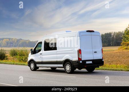 Furgone bianco o minibus viaggiando in autostrada a velocità in una bella giornata di autunno, cielo blu e nuvole bianche, vista posteriore. Foto Stock