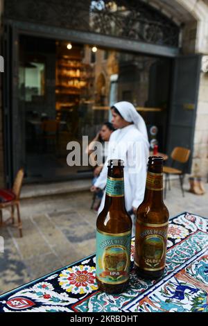 Gusterete una fredda birra palestinese Taybeh in una caffetteria/bar sulla vivace New Gate Street nel quartiere cristiano nella citta' vecchia di Gerusalemme. Foto Stock