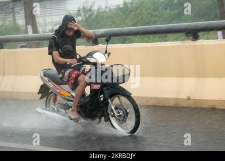 Ratchaburi, Thailandia, 14 2022 NOVEMBRE, Un giovane è in moto, scherzando gli occhi dalla pioggia pesante con la mano Foto Stock